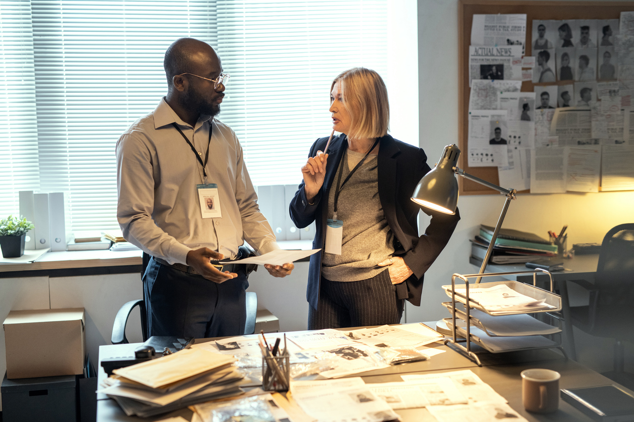 Two criminal investigators review files and documents in an office.