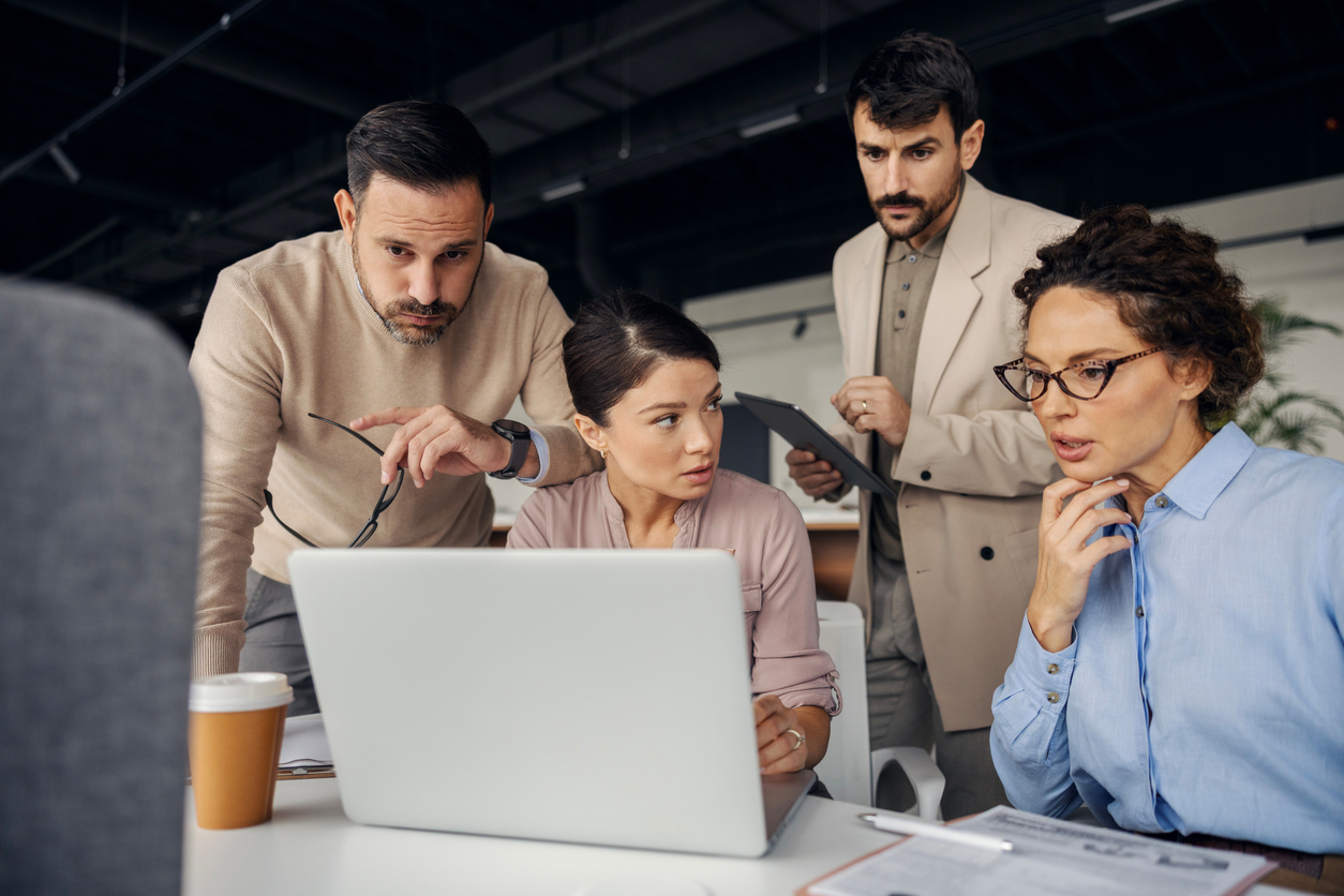 A crisis team meets in front of a laptop.