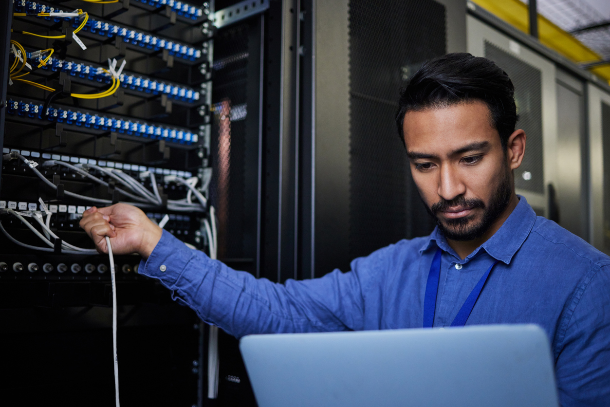 A cybersecurity professional working with a laptop in a control room. 