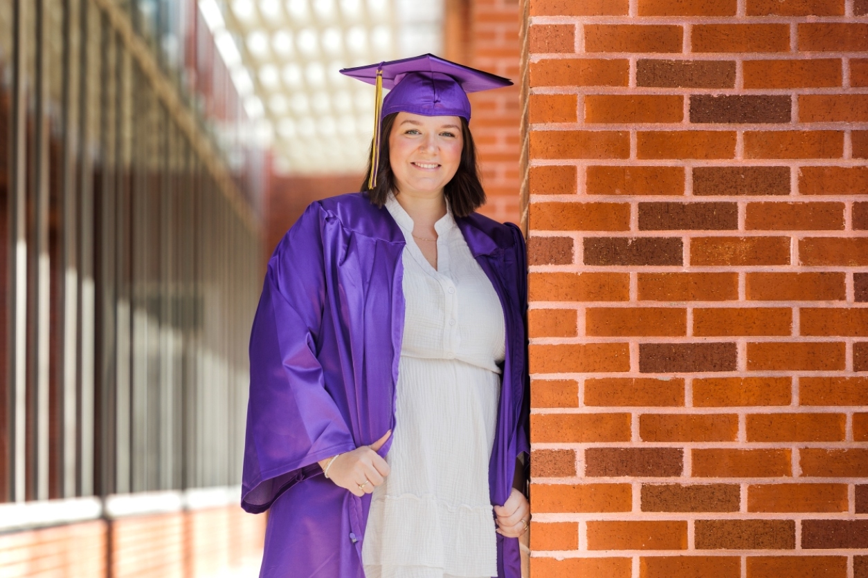 Sarah Branch in a cap and gown leaning on a brick wall. 