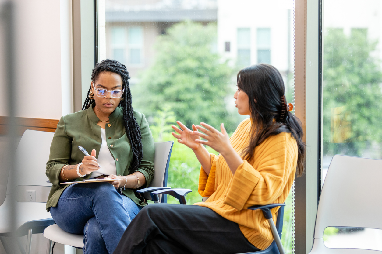 A mental health counselor takes notes on a clipboard while listening to a client.