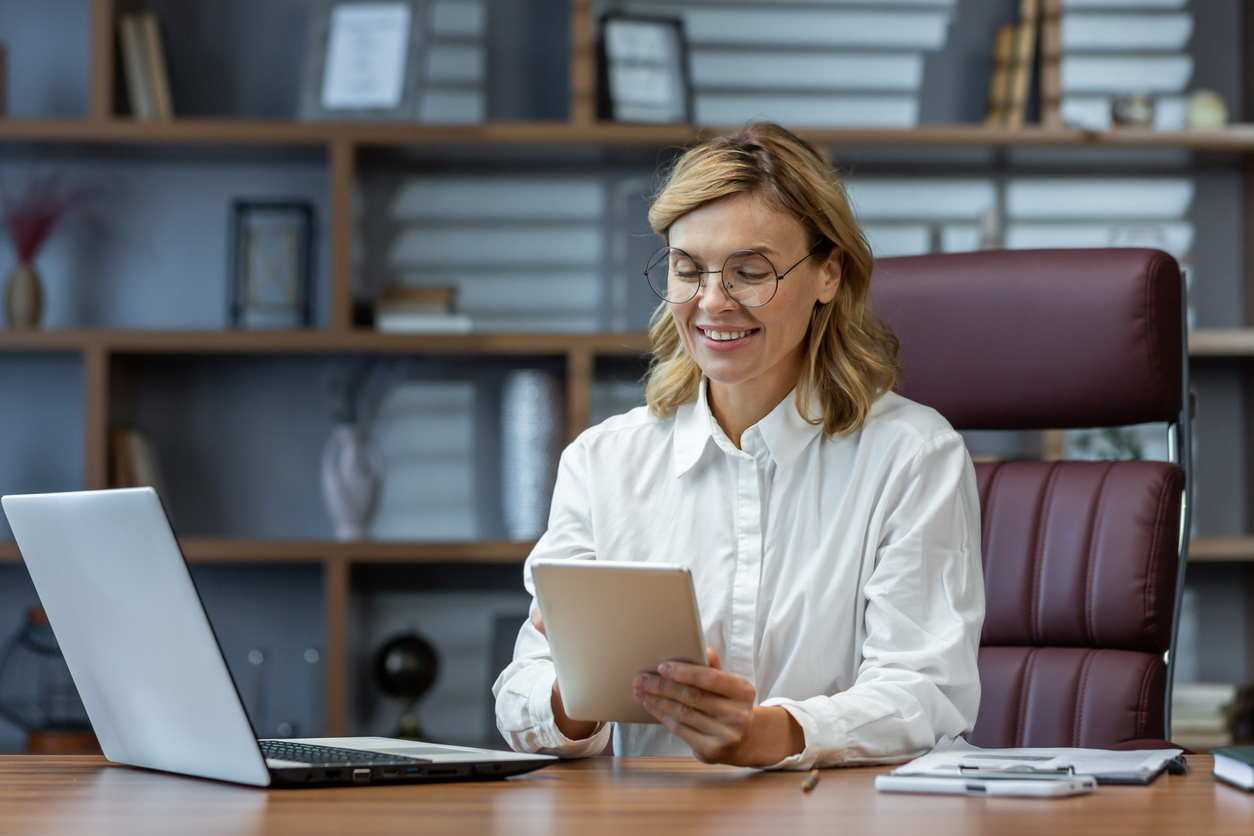 Organizational Psychologist Sitting at a Desk in an Office Looking at a Tablet.