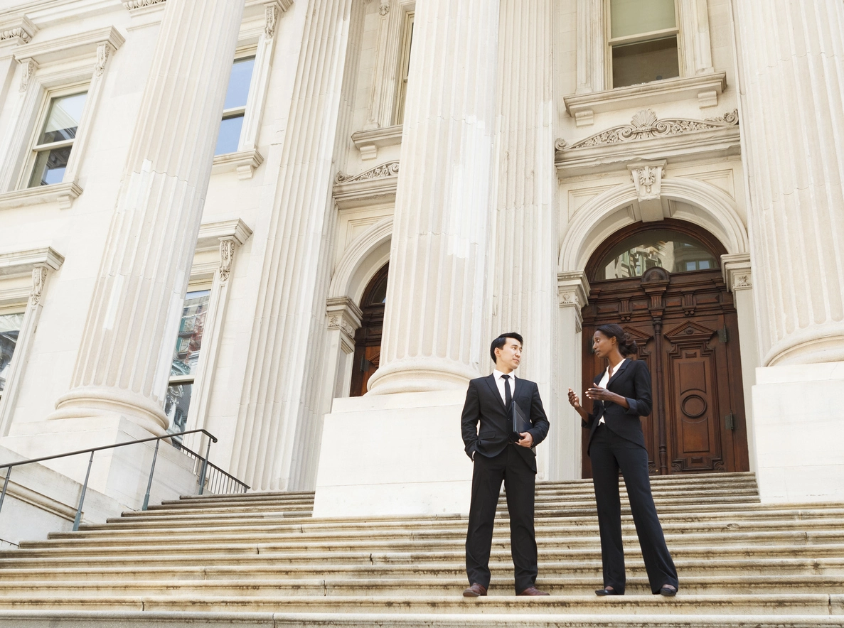 Two People Wearing Suits in Discussion While Standing on Courthouse Steps..webp
