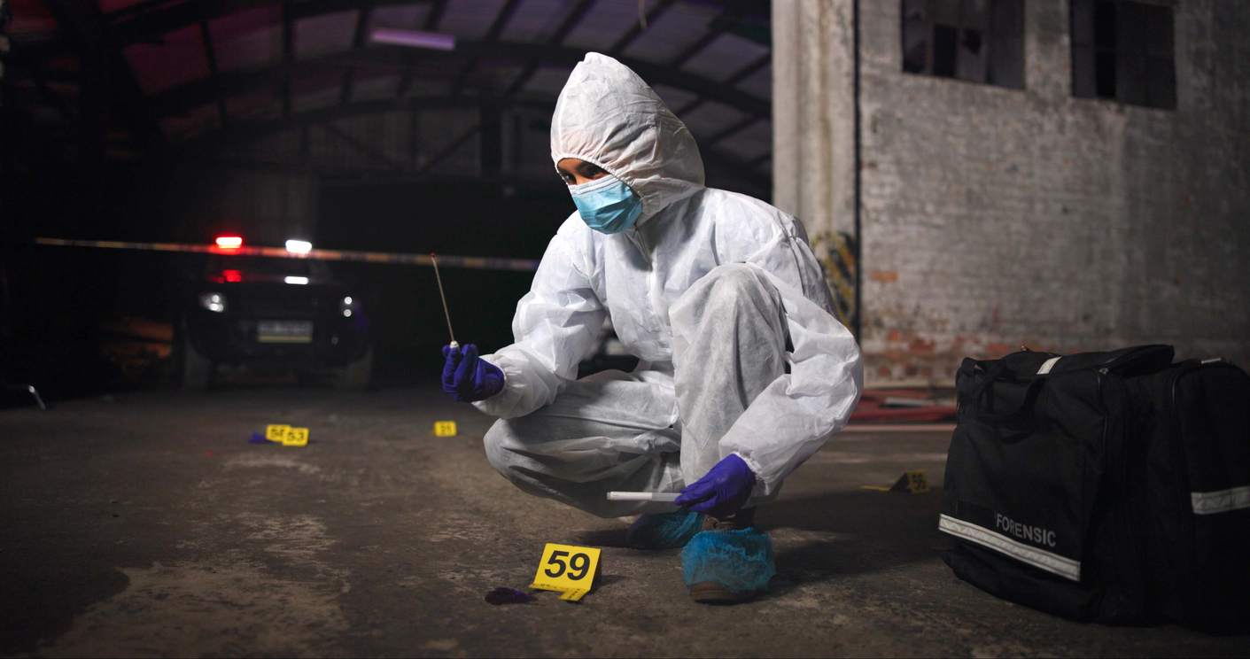 A CSI wearing personal protective equipment uses a swab taking a sample at a crime scene.