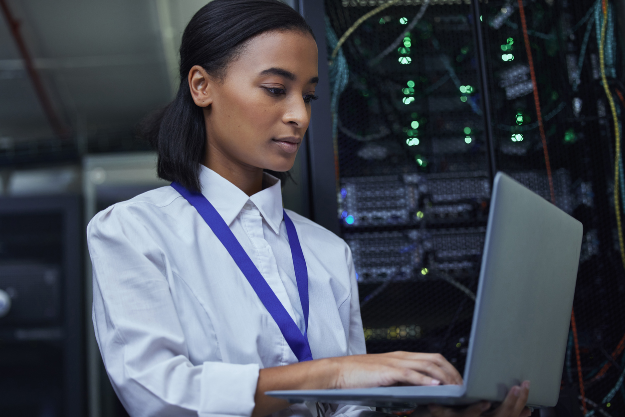A systems administrator works on a laptop in a server room.